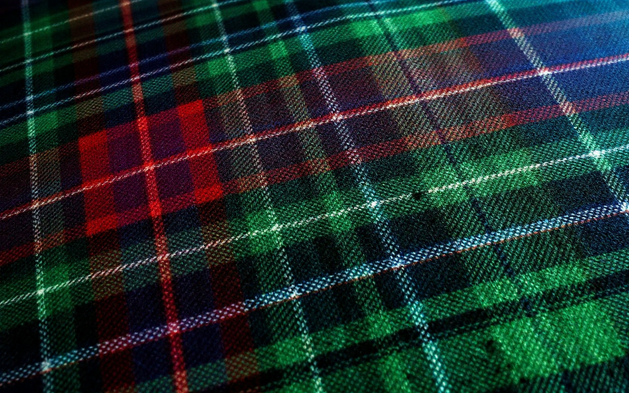 Gros plan sur un tissu tartan montrant des textures et des motifs colorés, avec des nuances de vert, rouge et bleu, mettant en évidence les détails du tissu.