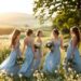demoiselles-dhonneur-en-robes-de-chiffon-bleu-poussiere-aux-silhouettes-fluides-reunies-dans-une-prairie-de-fleurs-sauvages-pres-dune-vieille-ferme-en-pierre-jupes-ondulant-sous-une-brise-leg