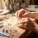 Mains féminines façonnant une bague en cire sur un établi d’atelier de bijouterie en Provence, entourées d’outils et de pierres colorées.